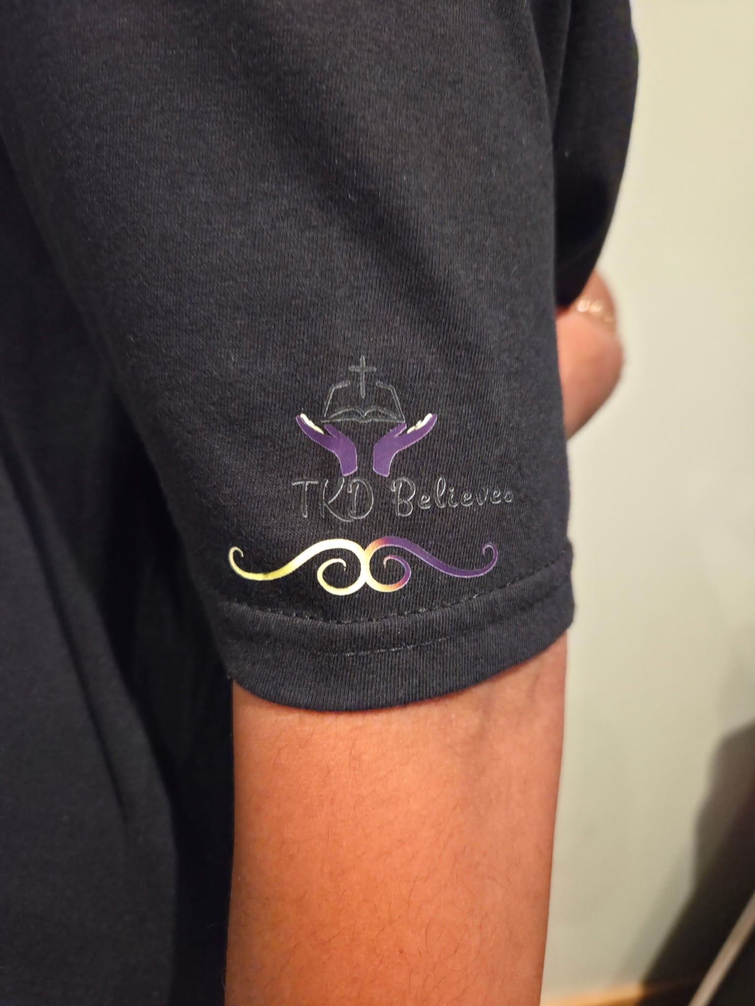 Close-up of TKD believes logo design on Essential Faith T-Shirt - Inspirational Christian clothing on arm
